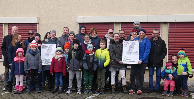 Ein Drittel der Gruppe «Eltern von Gansinger Kindern» mit ihren Jüngsten, die noch nicht an die Urne dürfen (im Hintergrund ist ein Teil eines grossen Risses am 80-jährigen Gansinger Schulhaus). Foto: zVg