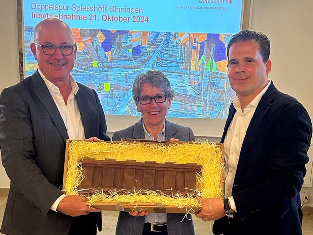 Mit einer symbolischen Tramschiene aus Schokolade übergibt Regierungspräsident Isaac Reber (links) die Doppelspur Spiesshöfli in Binningen an BLT-CEO Frédéric Monard (rechts). In der Mitte die Binninger Gemeindepräsidentin Caroline Rietschi. Foto: zVg